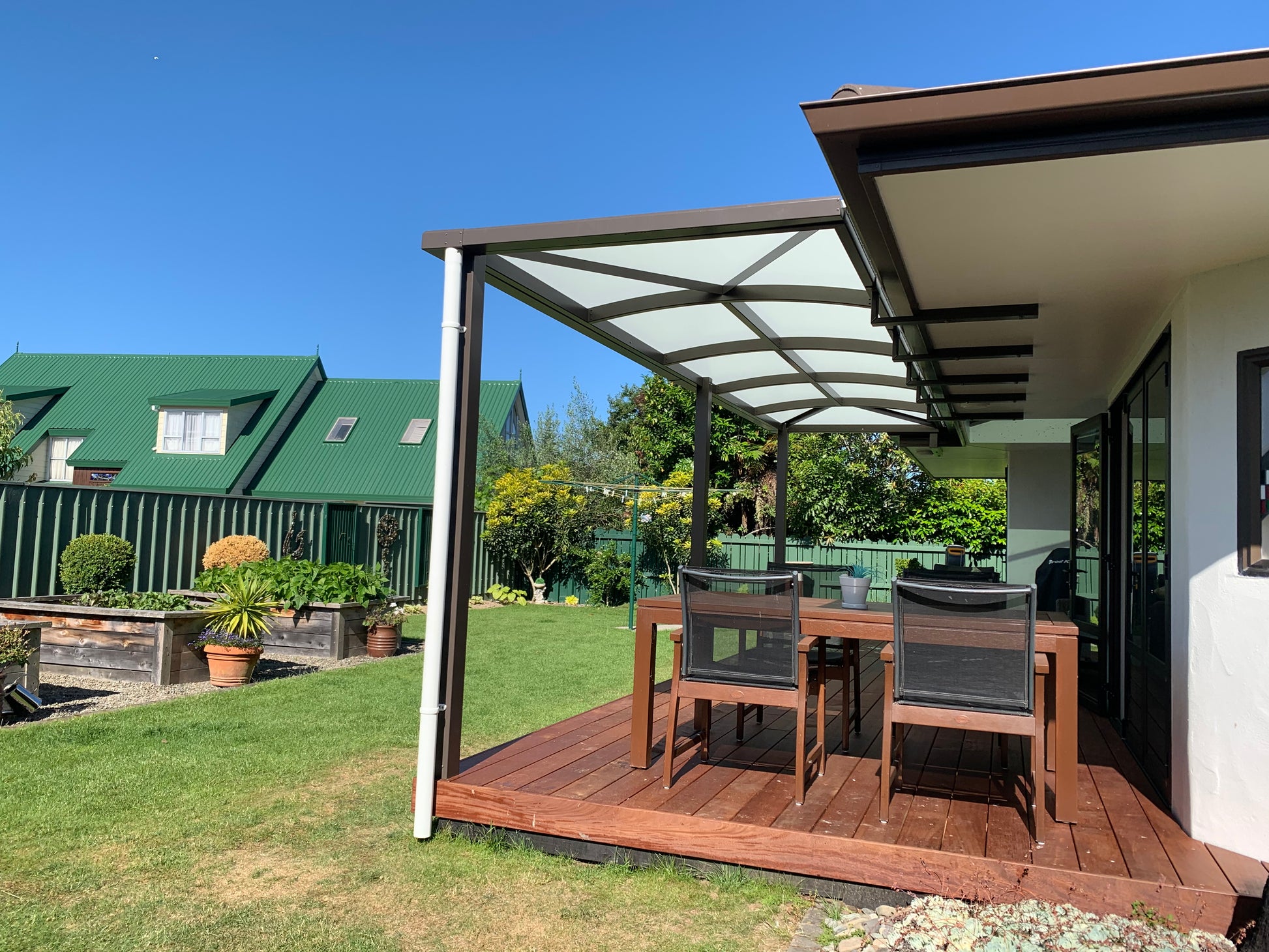 Outdoor patio area with wooden deck, table, and chairs under a pergola on a sunny day.